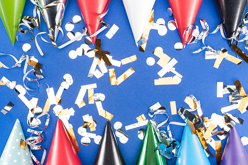 Colorful party hats and silver confetti on blue background