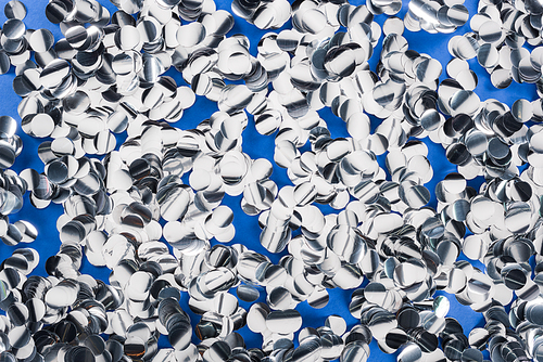 Top view of silver pieces of confetti on blue background