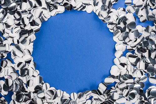 Top view of silver circle made of confetti on blue background
