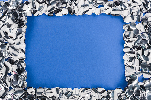 Top view of silver confetti frame on blue background