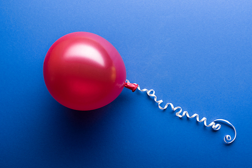 Top view of red balloon with white streamer on blue background
