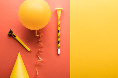 Top view of yellow balloon, streamer, party hat on coral and yellow background
