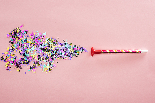 Party horn and multicolored confetti on pink background