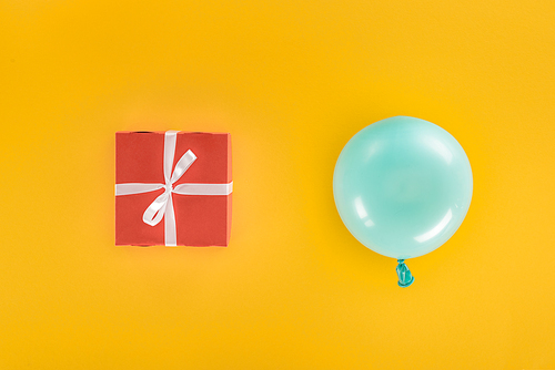 Top view of blue balloon and red gift box on yellow background