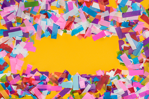 Top view of multicolored confetti frame on yellow background with copy space