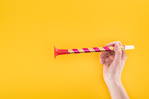 partial view of woman holding red party horn on yellow background
