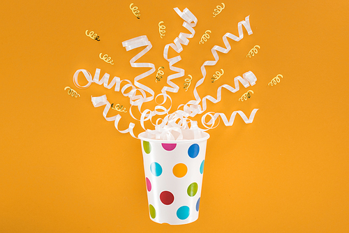 white and golden ribbons in polka dot cup on orange background