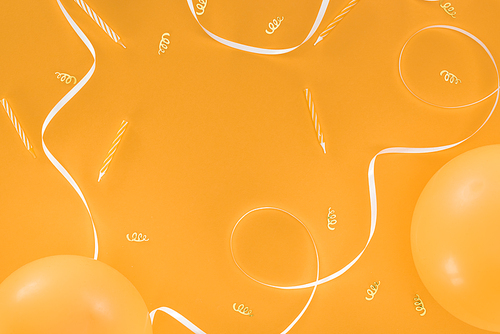 White ribbon and gold confetti and candles on orange background