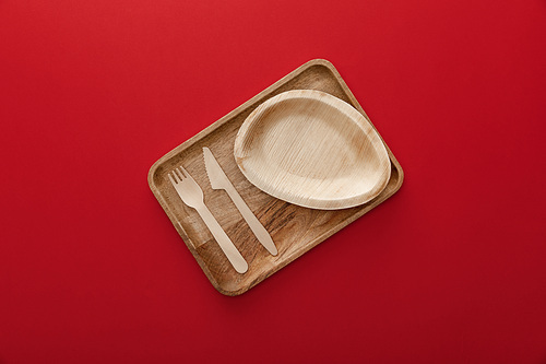 top view of natural rectangular wooden dish with plate, fork and knife on red background