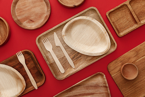 top view of eco-friendly wooden dishes, plates and cutlery on red background