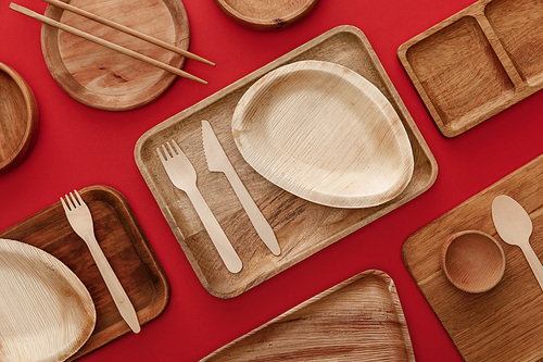 top view of eco-friendly wooden dishes, plates, chopsticks and cutlery on red background