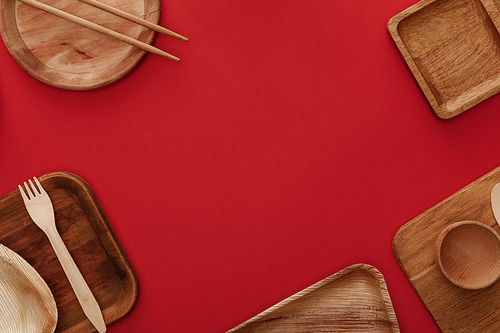 top view of wooden dishes, cup, fork and chopsticks on red background