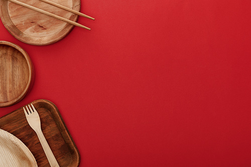 top view of wooden dishes with fork and chopsticks on red background