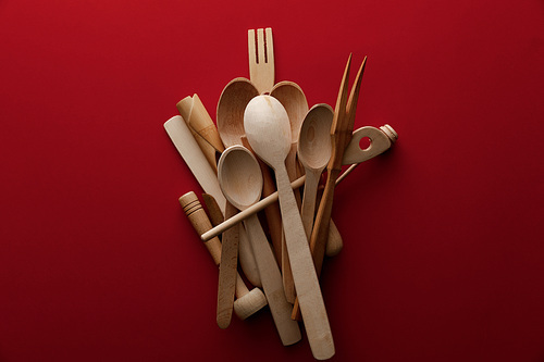 top view of eco-friendly wooden spoons, fork and kitchenware on red background
