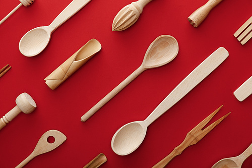 top view of natural wooden spoons, fork and kitchenware on red background