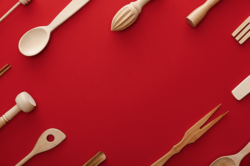 top view of natural wooden spoons, fork and kitchenware on red background with copy space