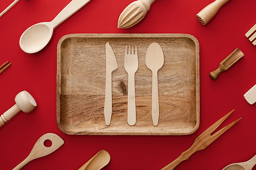 top view of natural rectangular wooden dish with cutlery on red background with kitchenware