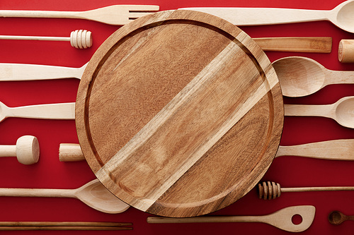 top view of round wooden cutting board on red background with kitchenware
