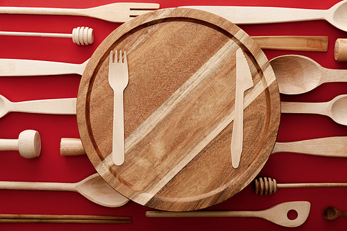 top view of round wooden cutting board with knife and fork on red background with kitchenware