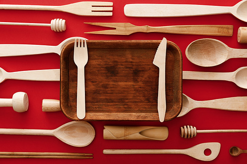 top view of rectangular wooden dish with knife and fork on red background with kitchenware