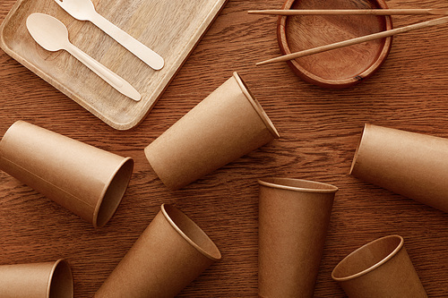 top view of wooden dishes, cutlery, chopsticks and paper cups on brown background