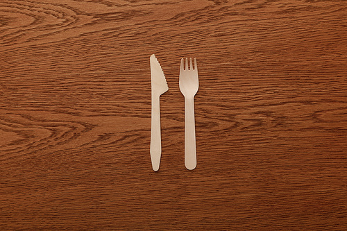 top view of wooden fork and knife on brown background