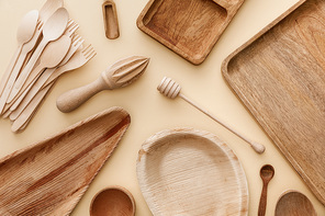 top view of wooden plates, dishes, forks, spoons and hand juicer on beige background