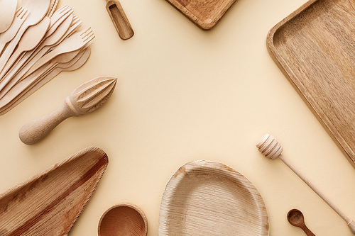 top view of wooden plates, dishes, forks, spoons and hand juicer on beige background with copy space