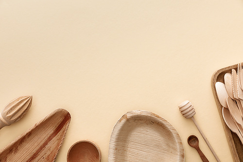 top view of wooden plates, spoons and hand juicer on beige background