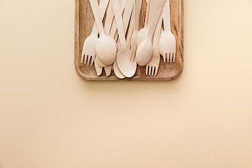 top view of rectangular wooden dish with forks, knifes and spoons on beige background