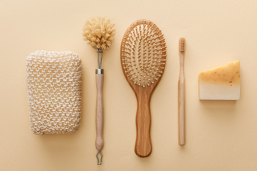 top view of natural bath sponge near toothbrush, hairbrush, body brush and soap on beige background