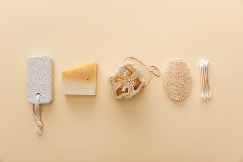 top view of natural soap near cotton swabs, loofah and pumice stone on beige background