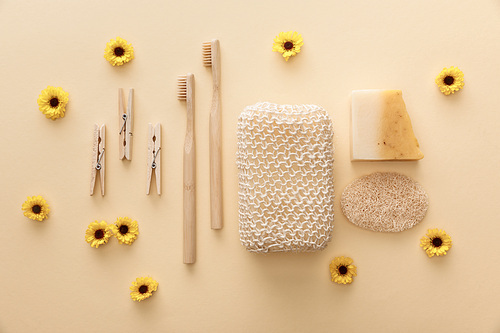 top view of wooden clothespins, toothbrushes, bath sponge, natural soap and loofah on beige background with flowers