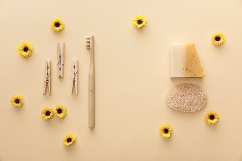 top view of wooden clothespins, toothbrush, natural soap and loofah on beige background with flowers
