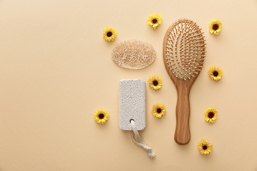 top view of wooden hairbrush, pumice stone and loofah on beige background with flowers