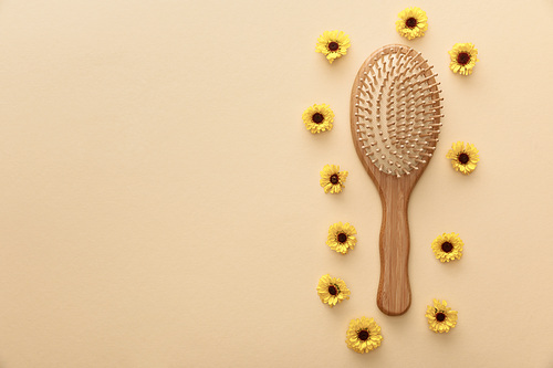 top view of wooden hairbrush on beige background with flowers