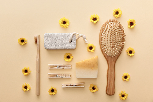 top view of wooden clothespins, toothbrush, hairbrush, pumice stone and piece of soap on beige background with flowers