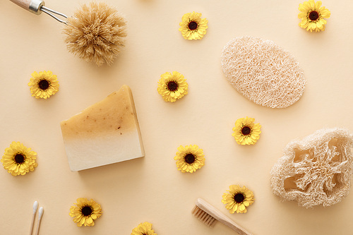 top view of loofah, cotton swabs, body brush, toothbrush and piece of soap on beige background with flowers