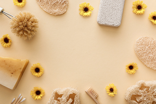 top view of loofah, cotton swabs, body brush, toothbrush and piece of soap on beige background with flowers and copy space