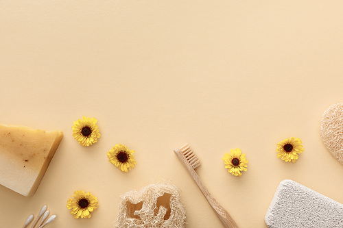 top view of loofah, cotton swabs, pumice stone, toothbrush and piece of soap on beige background with flowers