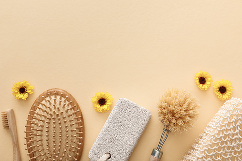 top view of toothbrush, hairbrush, body brush, bath sponge and pumice stone on beige background with flowers