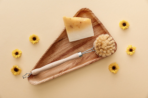 top view of triangle wooden dish with soap and body brush on beige background with flowers