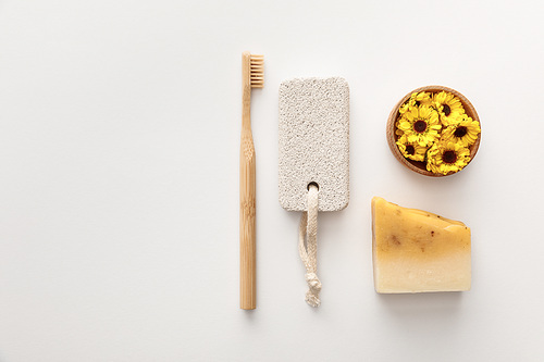 flat lay with toothbrush, piece of soap, pumice stone and cup with flowers on white background