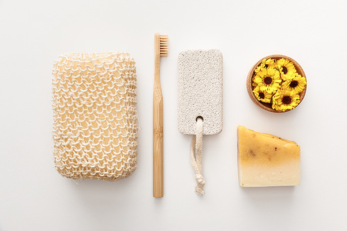 flat lay with bath sponge near toothbrush, piece of soap, pumice stone and cup with flowers on white background