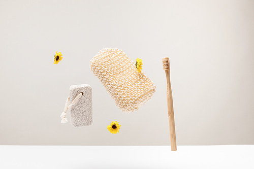 toothbrush, pumice stone, bath sponge and flowers isolated on gray