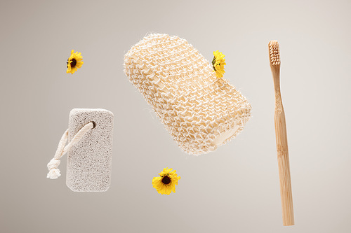 toothbrush, pumice stone, bath sponge and yellow flowers isolated on gray