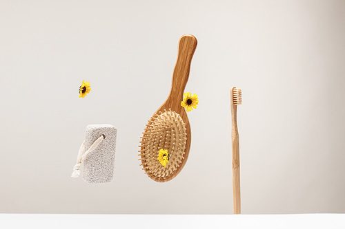 toothbrush, pumice stone, hairbrush and flowers isolated on gray