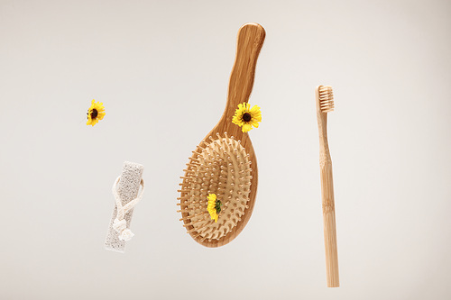 toothbrush, pumice stone, hairbrush and yellow flowers isolated on gray
