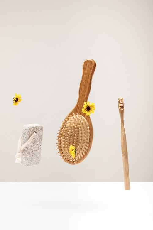 wooden toothbrush, pumice stone, hairbrush and flowers isolated on gray