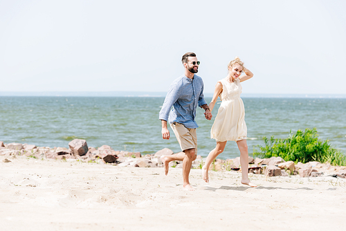 smiling young couple holding hands while running along beach